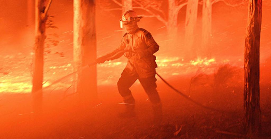 En brandman försöker släcka en markbrand i Australien.