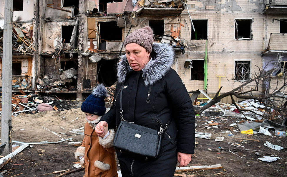 En kvinna med ett barn går förbi ett förstört bostadshus i en förstad till staden Kiev i Ukraina.