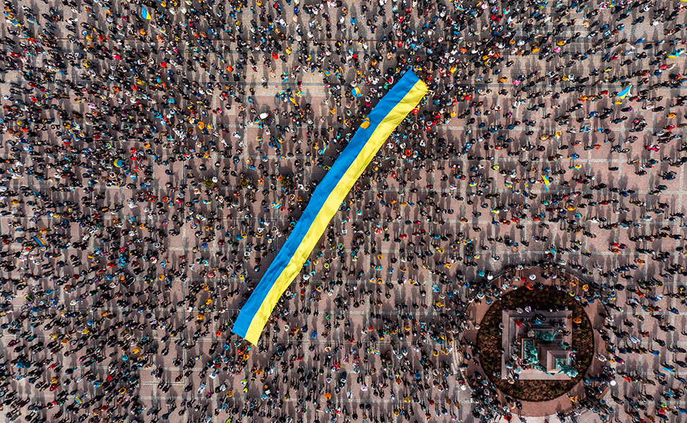 Bilden är ett flygfoto där flaggan och människorna är fotograferade uppifrån luften. Människorna bar Ukrainas flagga.