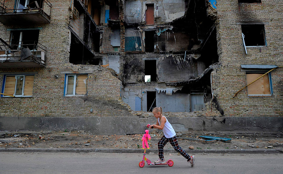 En flicka åkte sparkbräde förbi ett förstört bostadshus i byn Horenka i Ukraina.