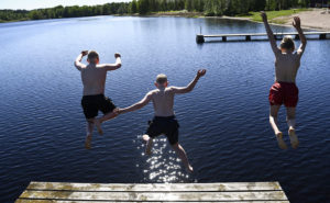 Tre män hoppar från en brygga i vattnet.
