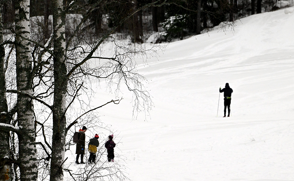 Utebild med snö. En person skidar och tre personer går.