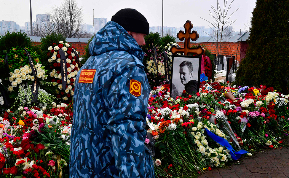 En säkerhetsvakt går förbi Aleksej Navalnyjs grav i Moskva. Graven är täckt av blommor och där finns ett fotografi av Aleksej Navalnyj.