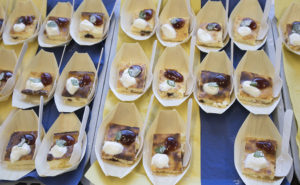 Små bitar av pannkaka med sylt som är upplagda på små engångsfat. Under faten finns servetter i blått och gult.