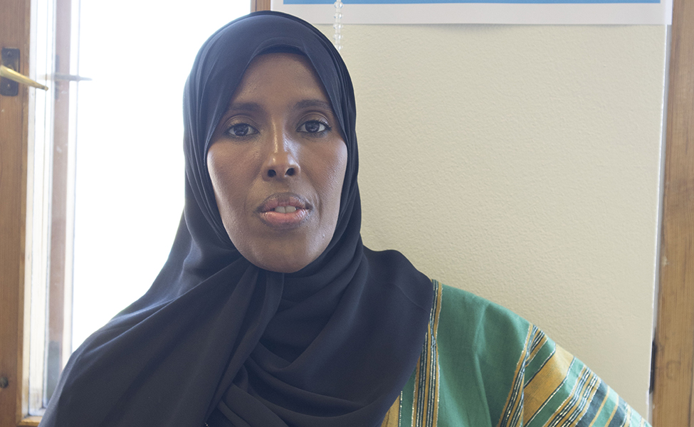 Bild av en somalisk kvinna med svart huvudduk och dräkt i grönt och guldfärg. Hon tittar mot kameran.