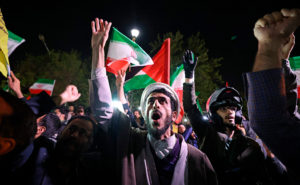 Bild på människor som viftar med ena handen i luften. Iranska flaggor syns på bilden.