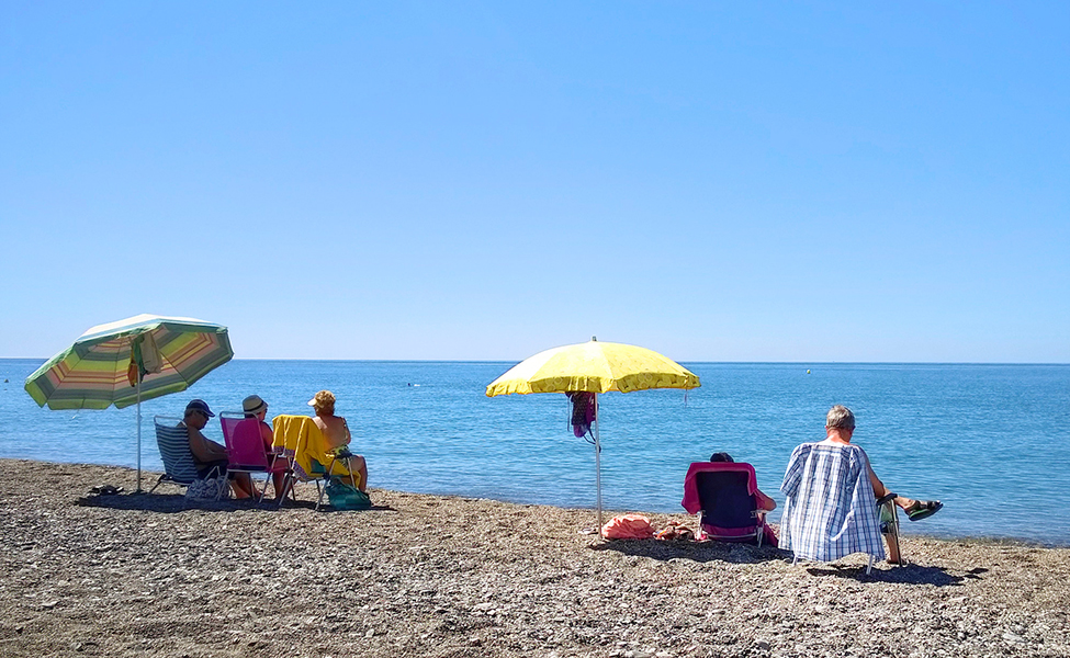 På stranden kan man sitta i skuggan under ett parasoll.