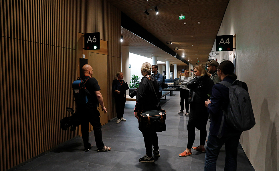 Flera journalister och fotografer med kameror som väntar vid en dörr inne i en byggnad.