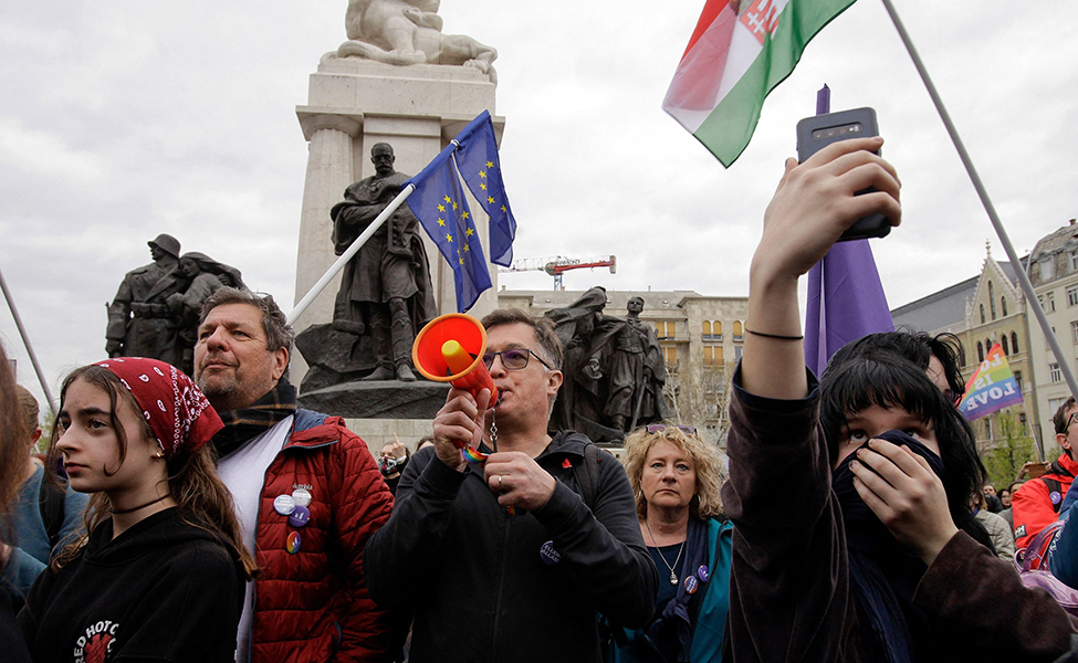 Människor som protesterar. En man håller i en megafon. På bilden syns också en EU-flagga, Ungerns flagga och en regnbågsflagga.