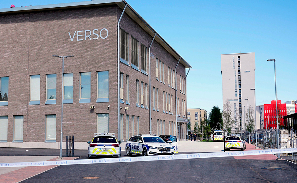 En bild av en skolbygnad. Runt omkring skolan står flera polisbilar.