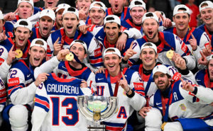 Många manliga ishockeyspelare som har samlats för ett gruppfoto. De har USA:s landslagsdress på sig och har guldmedaljer som hänger runt halsen eller som de håller i och visar upp för fotografen.