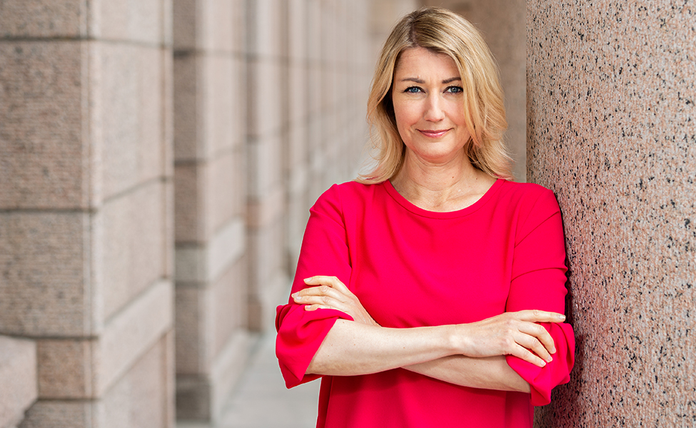 Politikerm Maria Guzenina. Hon håller armarna i kors, och är klädd i rött.