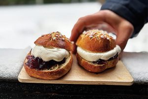 Två bullar som är fyllda med sylt och grädde. En hand sträcks fram mot en av bullarna.