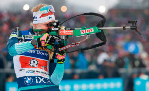 En kvinna i idrottskläder håller i ett skidkyttegevär och siktar mot målet.