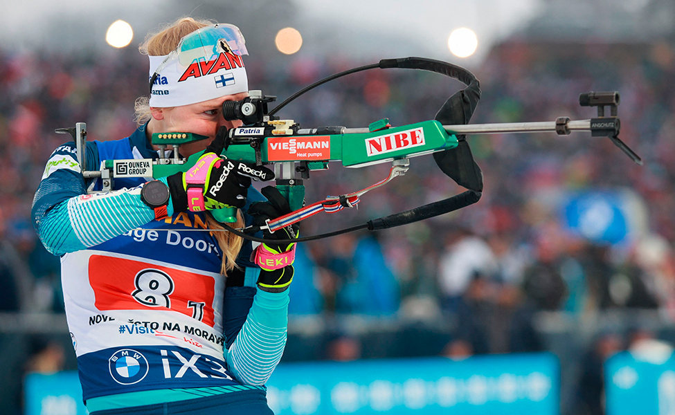 En kvinna i idrottskläder håller i ett skidkyttegevär och siktar mot målet.